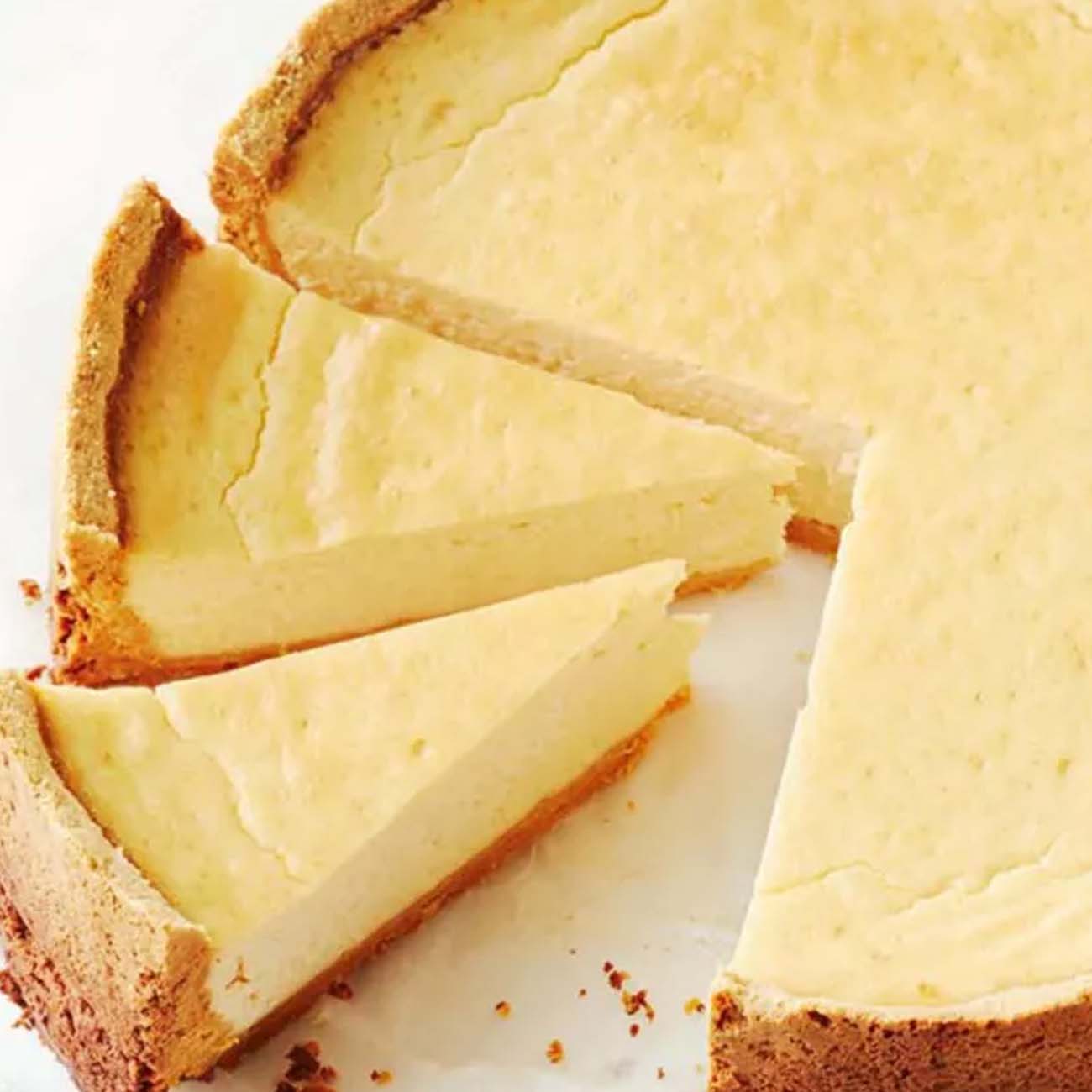 A classic baked New York cheesecake on a white surface, cut into slices to show the smooth texture and crumbly biscuit crust.