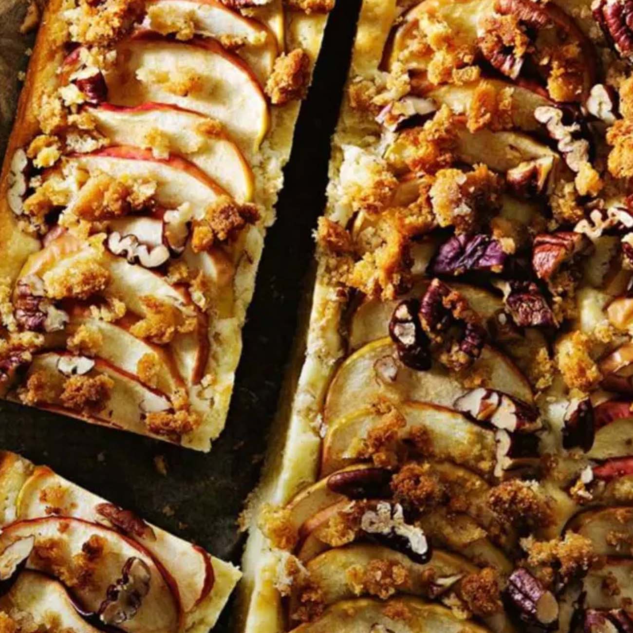 A rustic apple tart topped with overlapping apple slices, chopped pecans and a golden brown crumble topping.