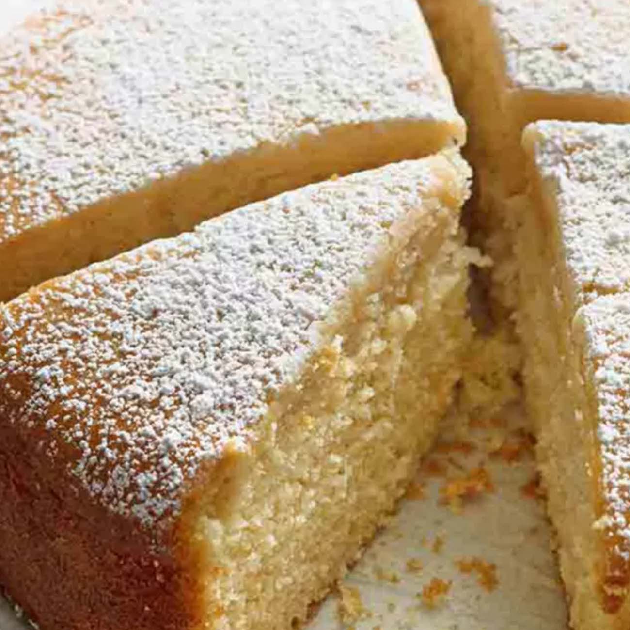 A simple, golden butter cake cut into slices and heavily dusted with powdered icing sugar on top.